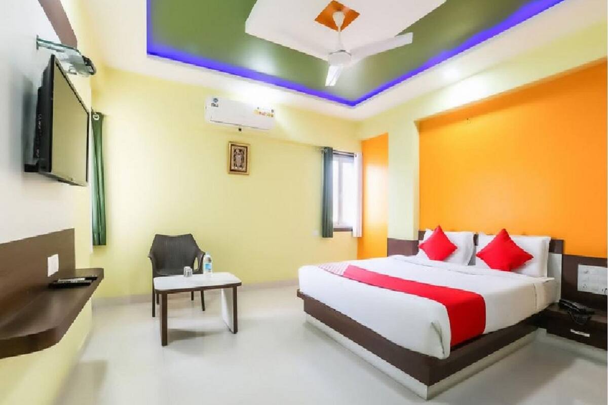 A hotel room with a bed, a desk, a chair, a TV, and an air conditioning unit.