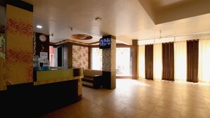 A hotel lobby with a reception desk, a sofa, and a large window with curtains. - Hotel Atithi Bhawan by Sky Stays (Nathdwara)