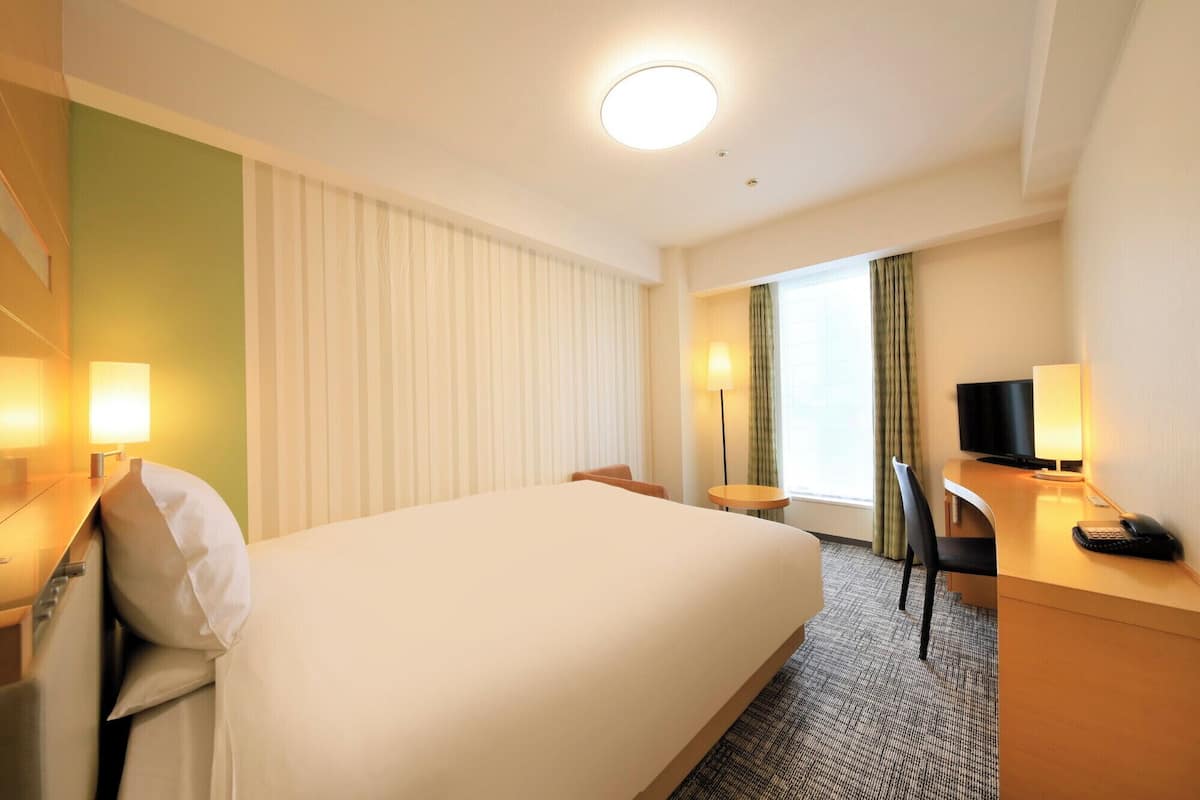A hotel room with a large bed, a desk with a computer, a chair, and a TV.