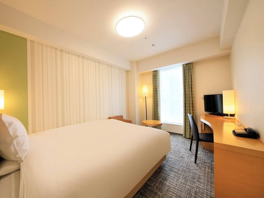 A hotel room with a large bed, a desk with a computer, a chair, and a TV.
