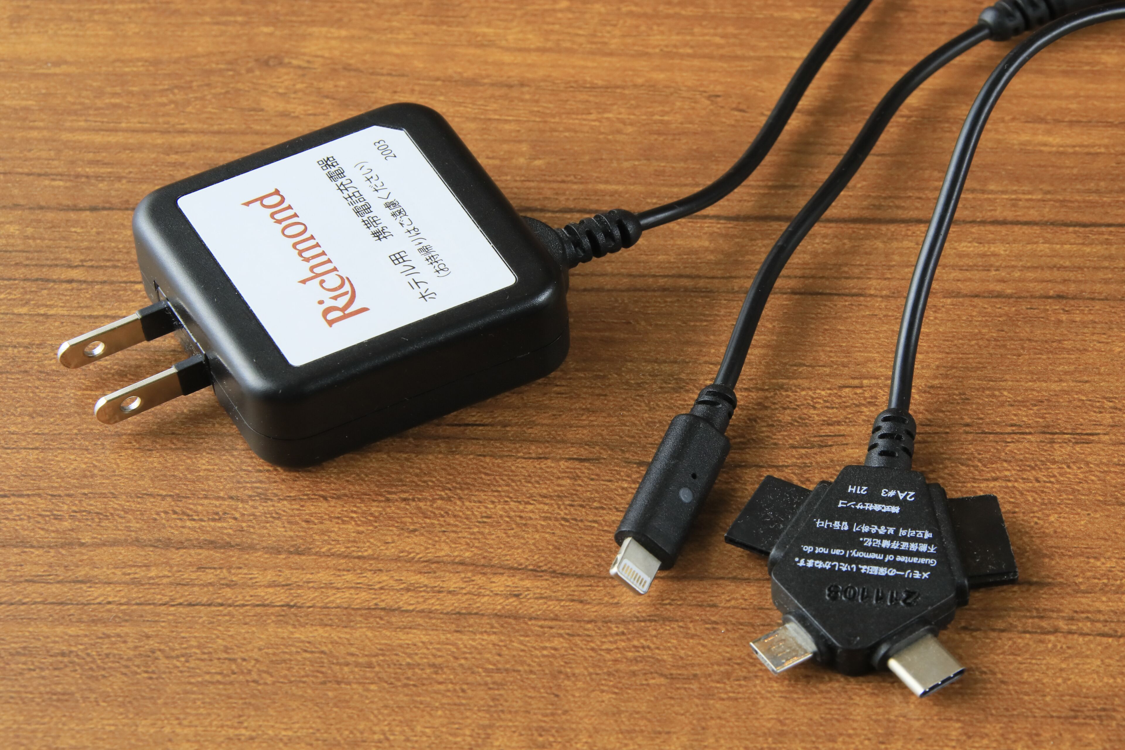 A black power adapter with a white label and two USB cables on a wooden surface.