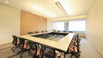 A conference room with a long table, chairs, and a view of the outdoors through large windows.