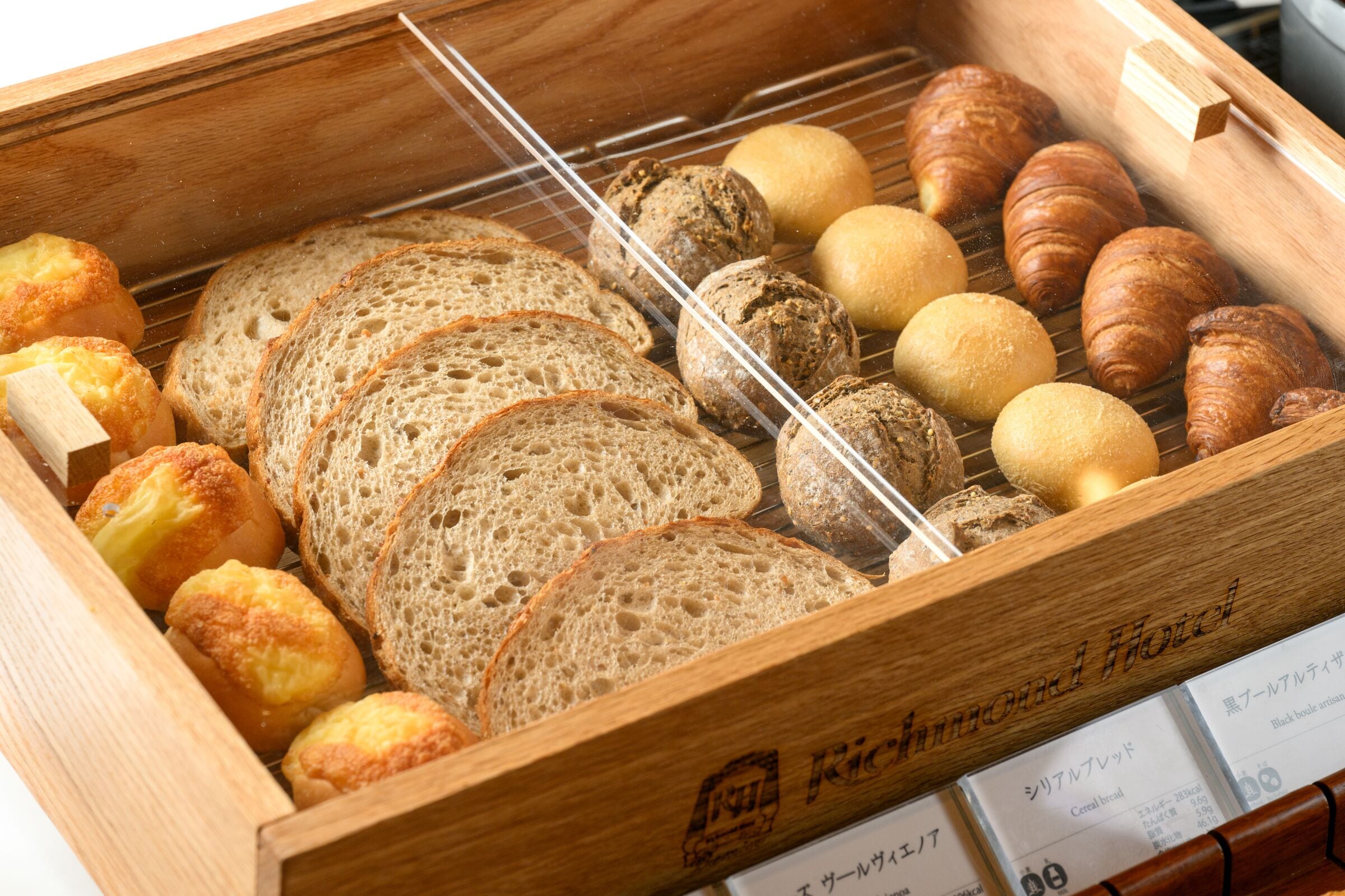 Una vetrina in legno esposta con diversi prodotti da forno, tra cui pane, croissant e pasticcini.