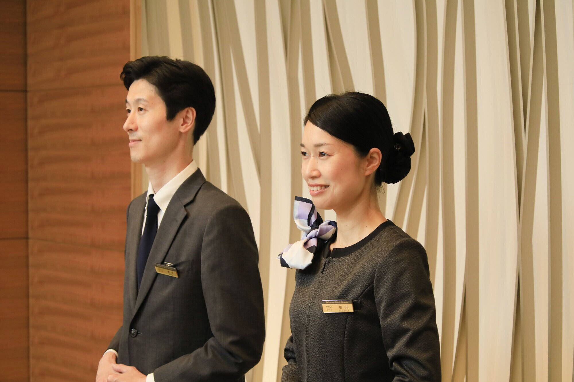Two individuals standing in front of a curtain.