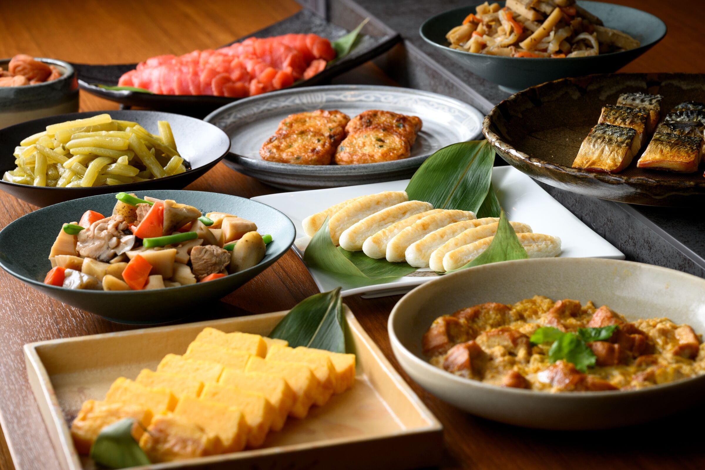 A variety of dishes on a table, including what appears to be a bowl of soup, a plate of noodles, and several other dishes with different ingredients.