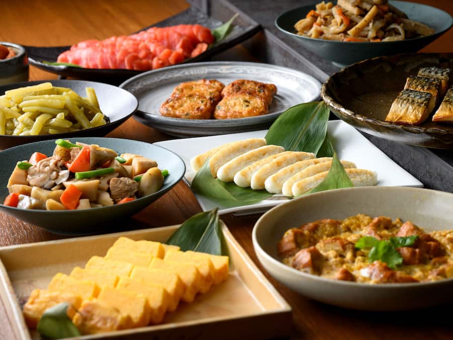 A variety of dishes on a table, including what appears to be a bowl of soup, a plate of noodles, and several other dishes with different ingredients.