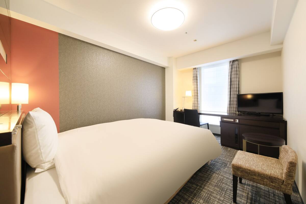 A hotel room with a large bed, a desk with a computer, a TV, and a chair.