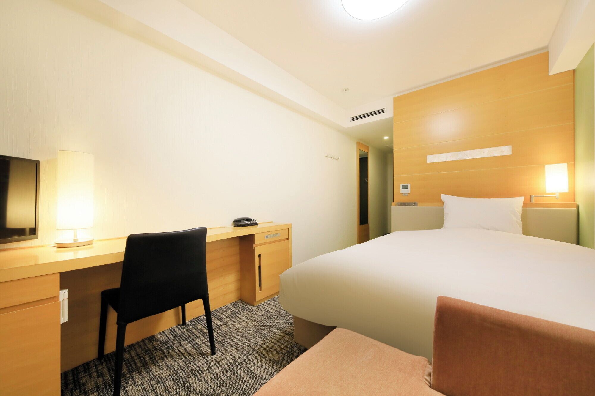 Een hotelkamer met een bed, een bureau, een stoel, een televisie en een lamp.