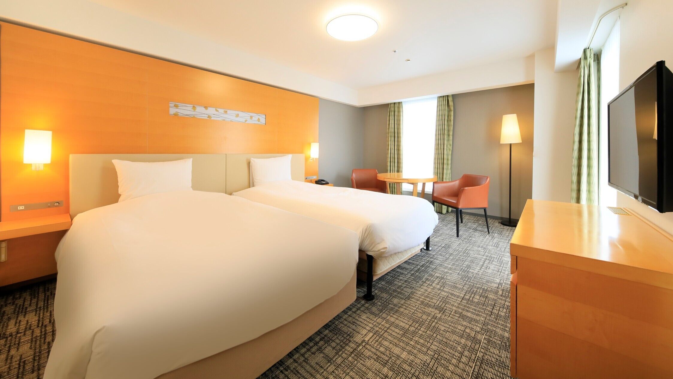 A hotel room with two beds, a desk, a chair, a TV, and a window with curtains.