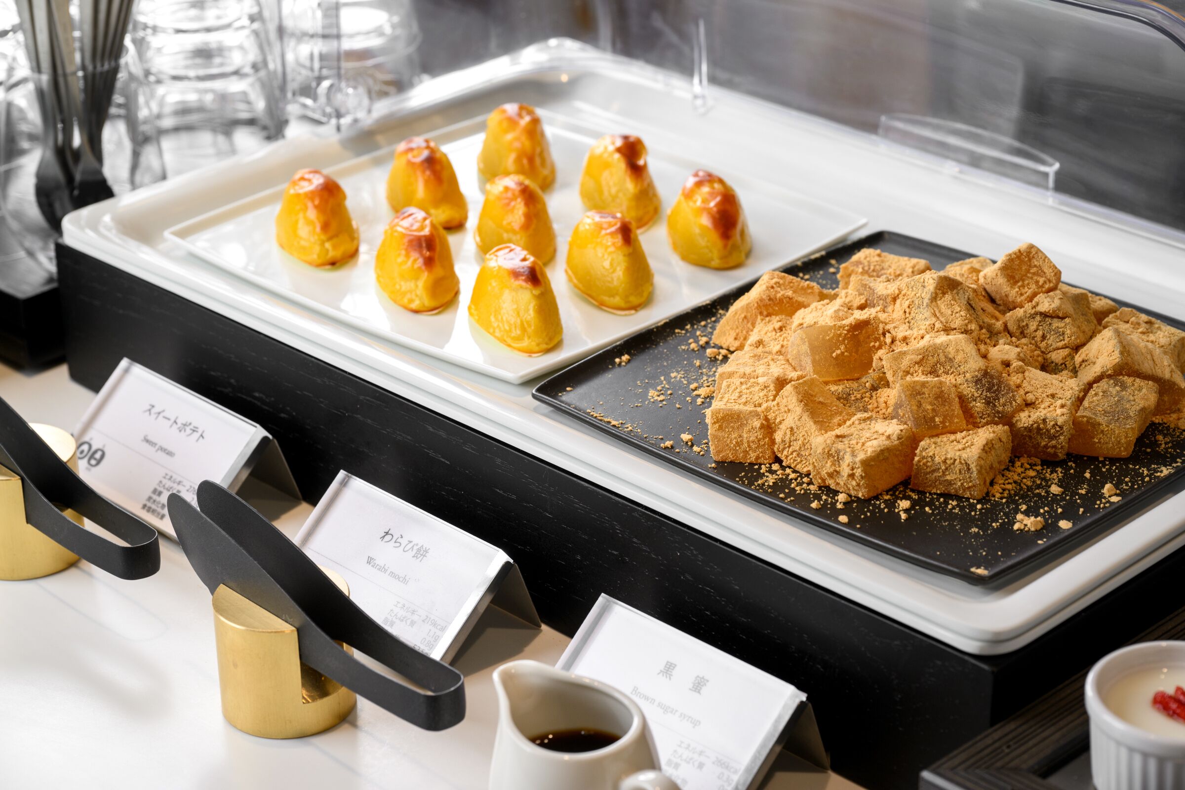 Ein Buffet mit verschiedenen Speisen, darunter eine Platte mit goldbraunen Würfeln und eine Auswahl an Süßspeisen.
