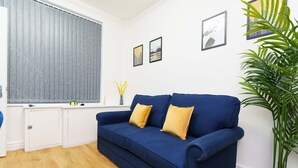 A living room with a blue sofa, two yellow cushions, a potted plant, and framed pictures on the wall. - Spencer House (Leeds)