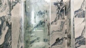 A glass-enclosed shower with marble walls and floor. - Spencer House (Leeds)