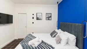 A modern hotel room with a large bed, a flat-screen TV mounted on the wall, and a blue accent wall. - Spencer House (Leeds)