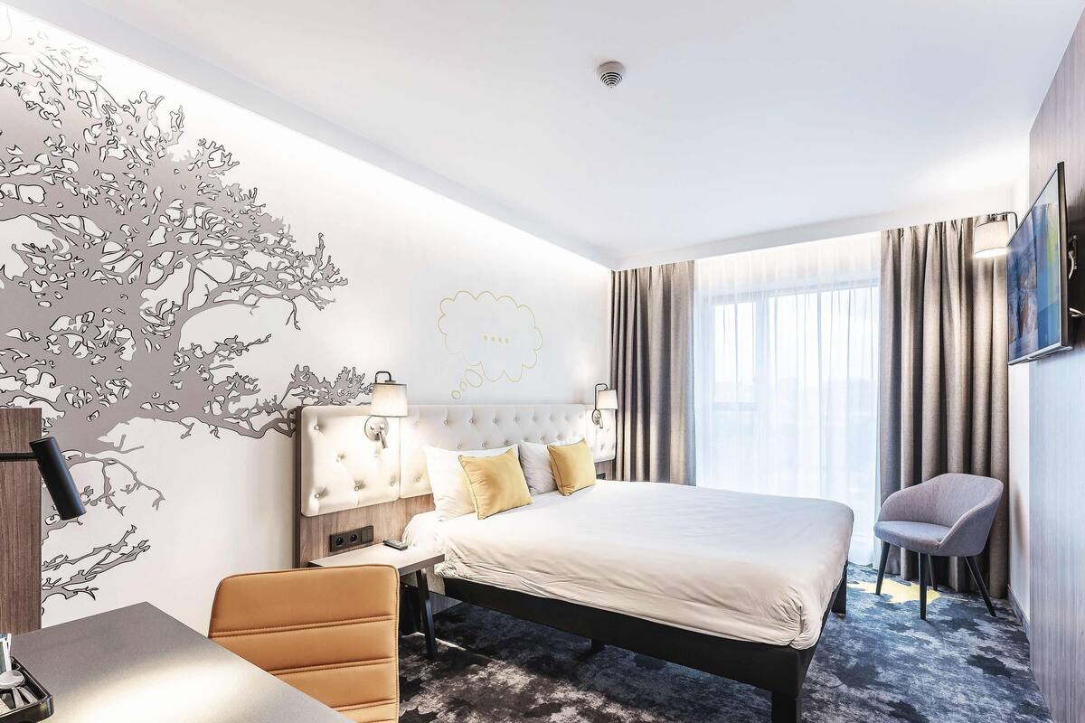 Ein modernes Hotelzimmer mit einem großen Bett, einem Schreibtisch, einem Sessel und einem Wandbild.
