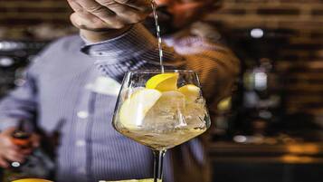 Un barman verse une boisson dans un verre rempli de glaçons et garni de rondelles de citron.