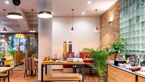 A modern dining area with a wooden floor, a central table with a buffet, red upholstered seating, and hanging pendant lights. - ibis Styles Lublin Stare Miasto (Lublin)