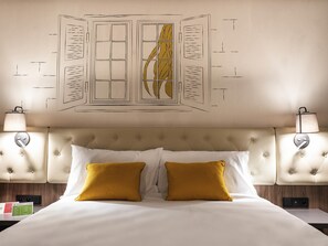 A hotel room with a tufted headboard, two bedside lamps, a bed with white and mustard pillows, and a wall art piece above the bed. - ibis Styles Lublin Stare Miasto (Lublin)