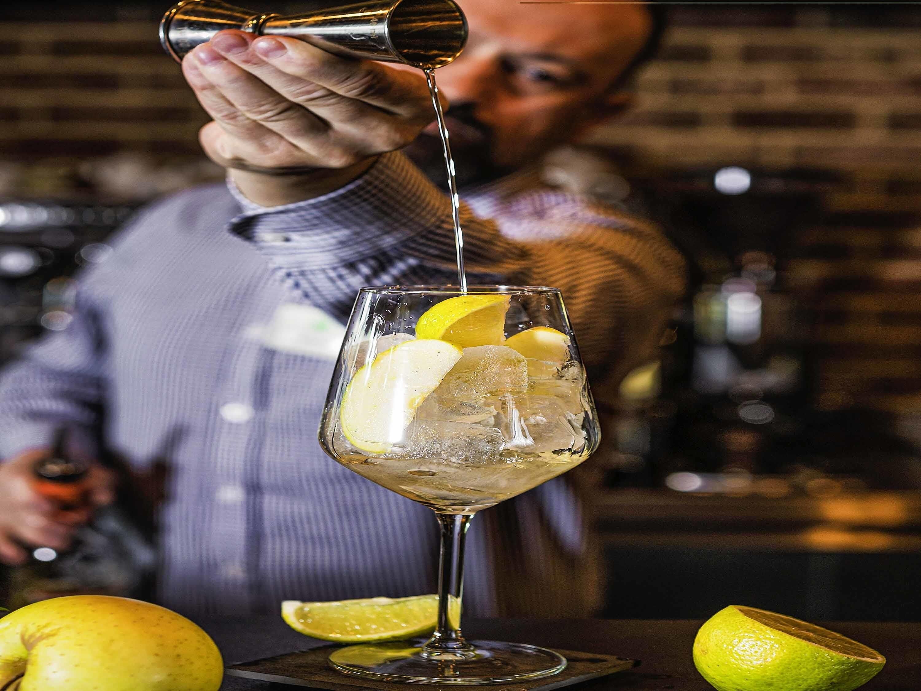A bartender pouring a drink into a glass with ice and lemon slices.