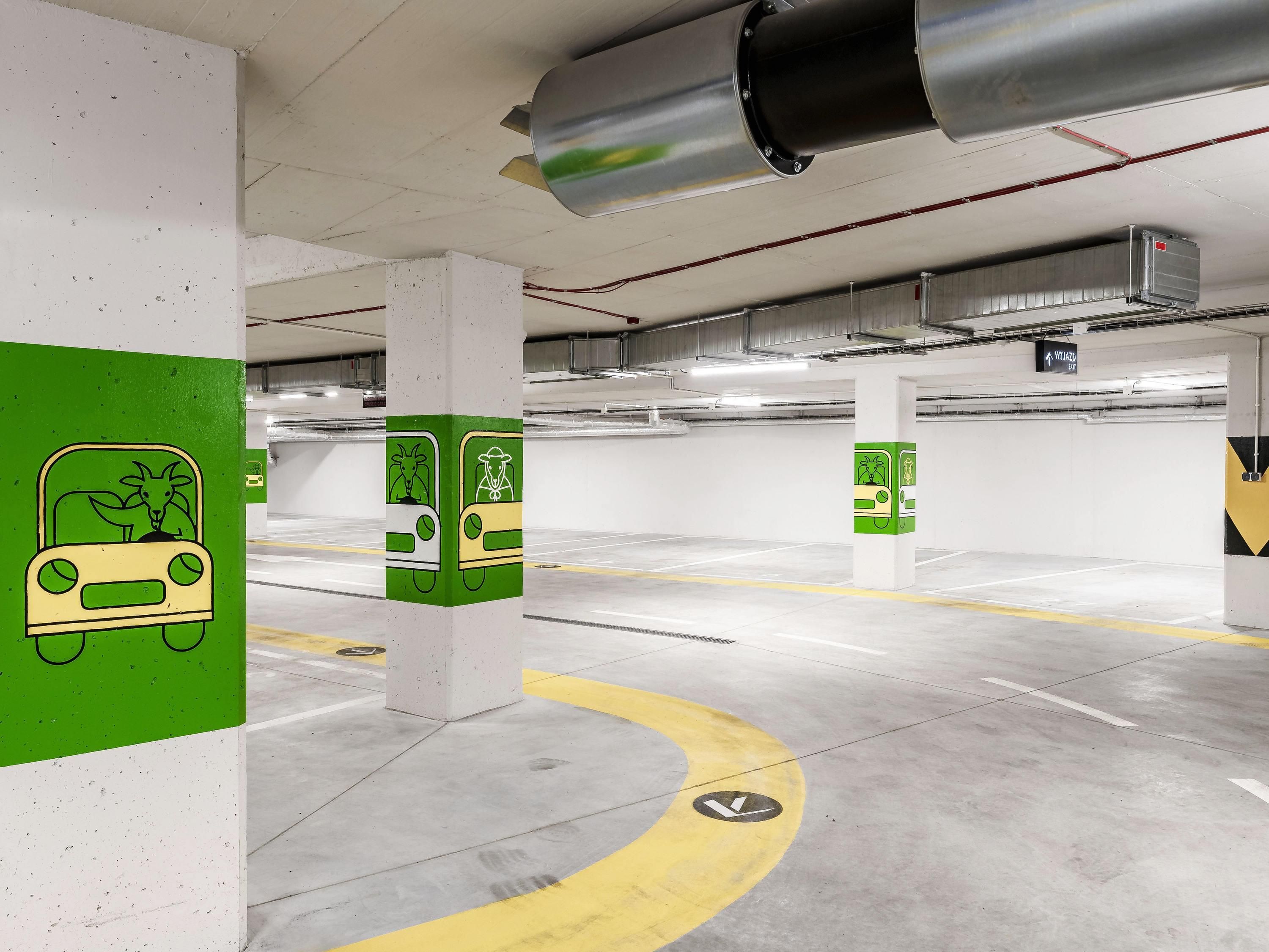 A parking garage with green and white pillars, directional arrows on the floor, and a ventilation system.