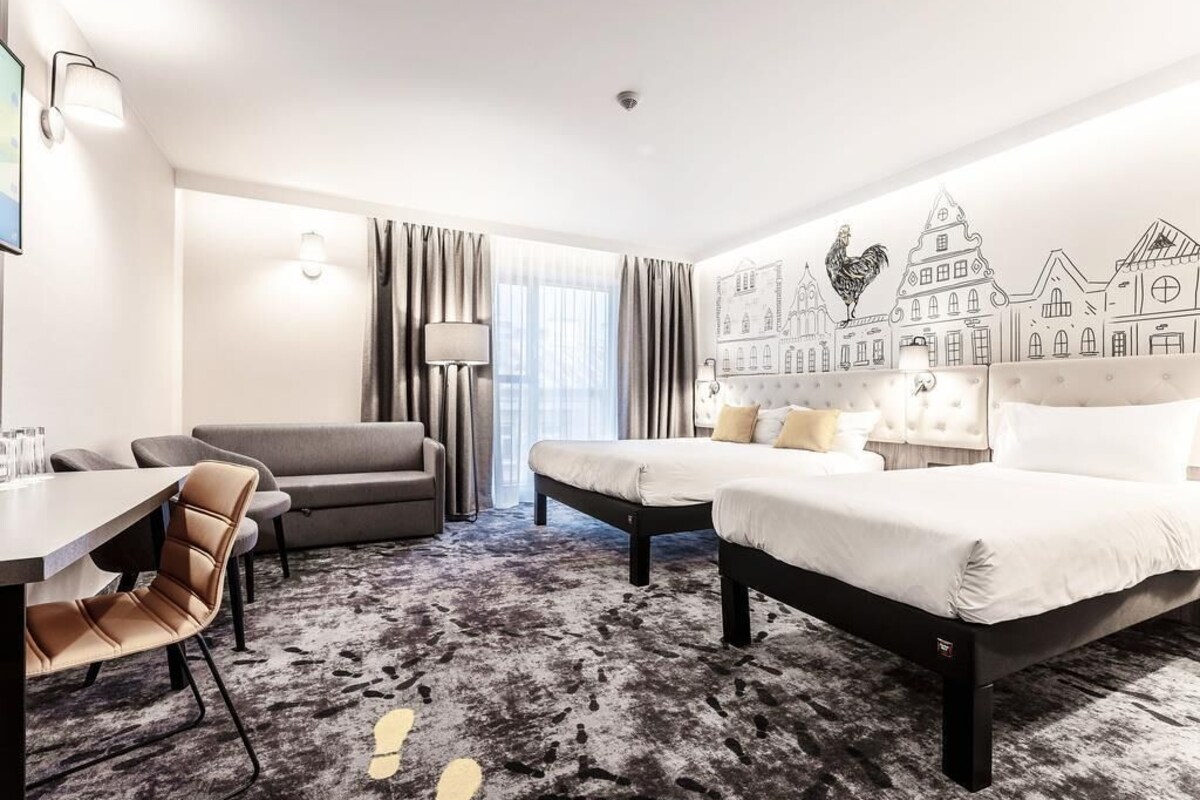A hotel room with a bed, a sofa, a desk, and a lamp.