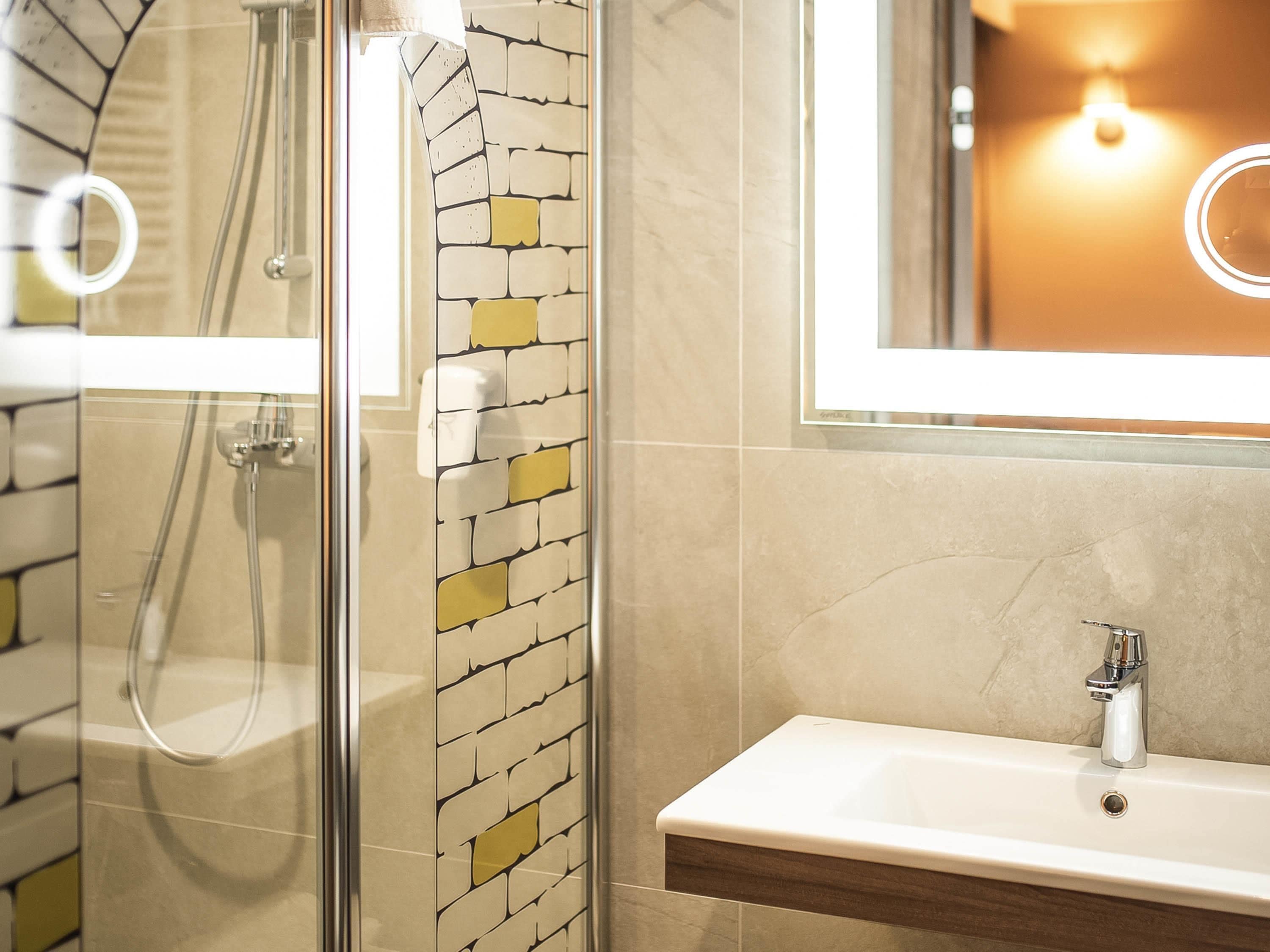 A bathroom with a glass shower enclosure, a white sink, and a mirror with a light fixture.