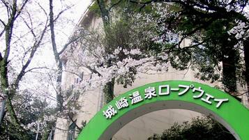 A green archway with Japanese text, leading to a staircase surrounded by trees and greenery.