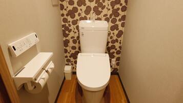 A small bathroom with a toilet, a paper towel dispenser, and a wall-mounted electrical outlet.