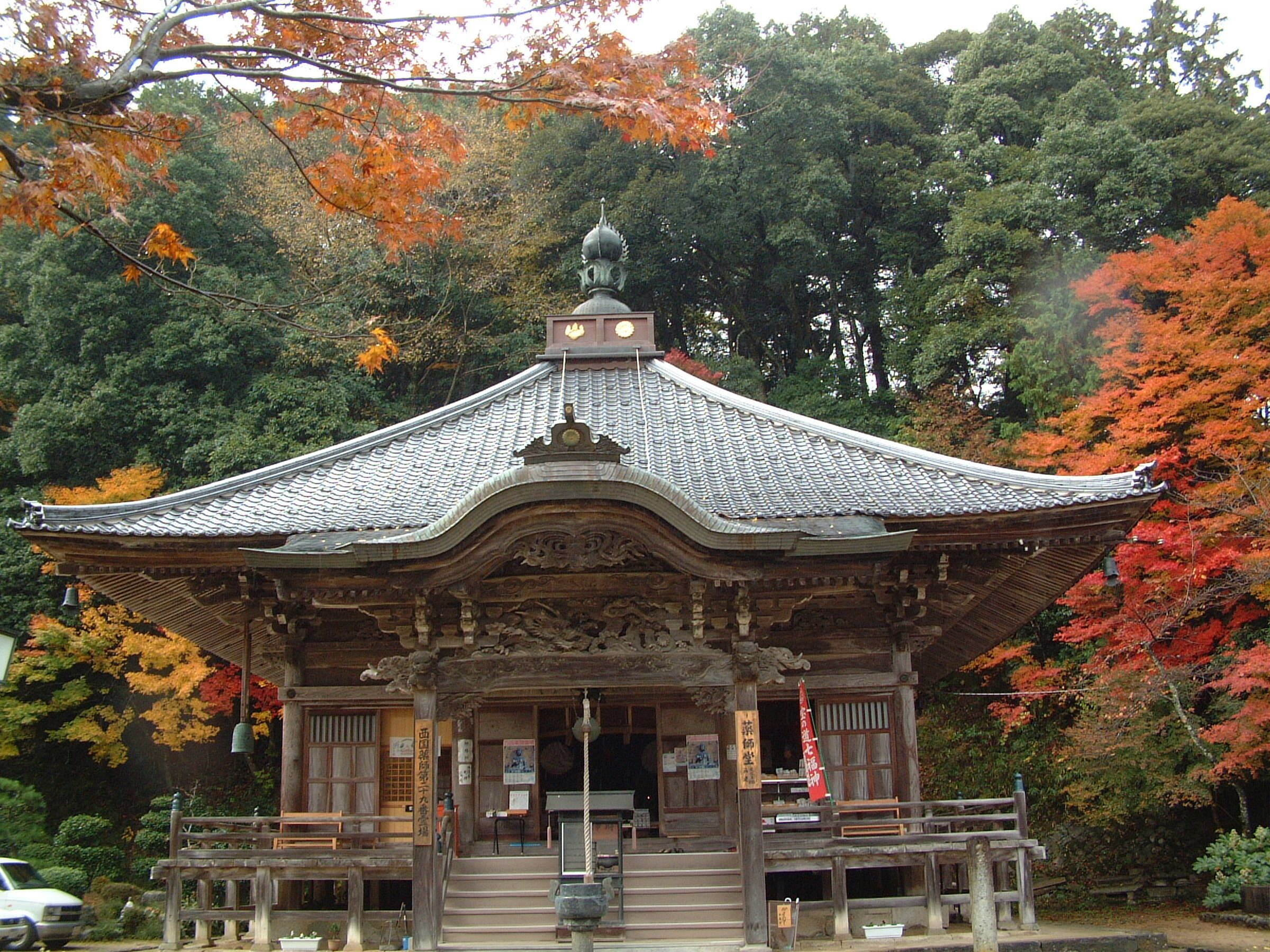 A traditional Japanese temple with a tiled roof and wooden structure, surrounded by autumn foliage.