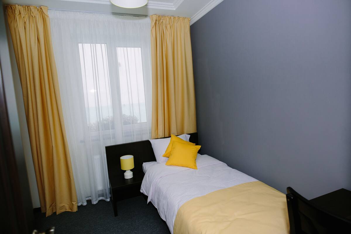 A hotel room with a bed, a nightstand, a lamp, and curtains.