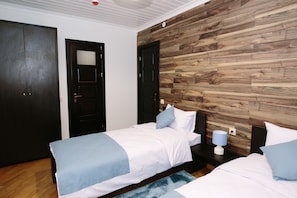 Un dormitorio con dos camas individuales, una pared decorativa de madera, una puerta oscura y una mesita de noche con una lámpara.