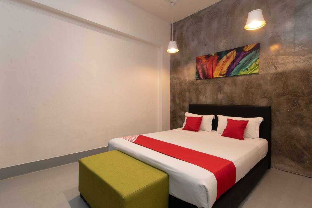 Une chambre d’hôtel moderne avec un grand lit, un pouf vert et un tableau abstrait aux couleurs vives accroché au mur.