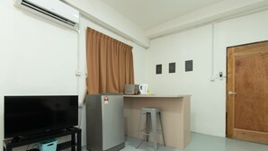 A compact living space with a kitchenette, a refrigerator, a small bar area, a television, and a wooden door. - OYO 43993 Madsuite (Kota Kinabalu)