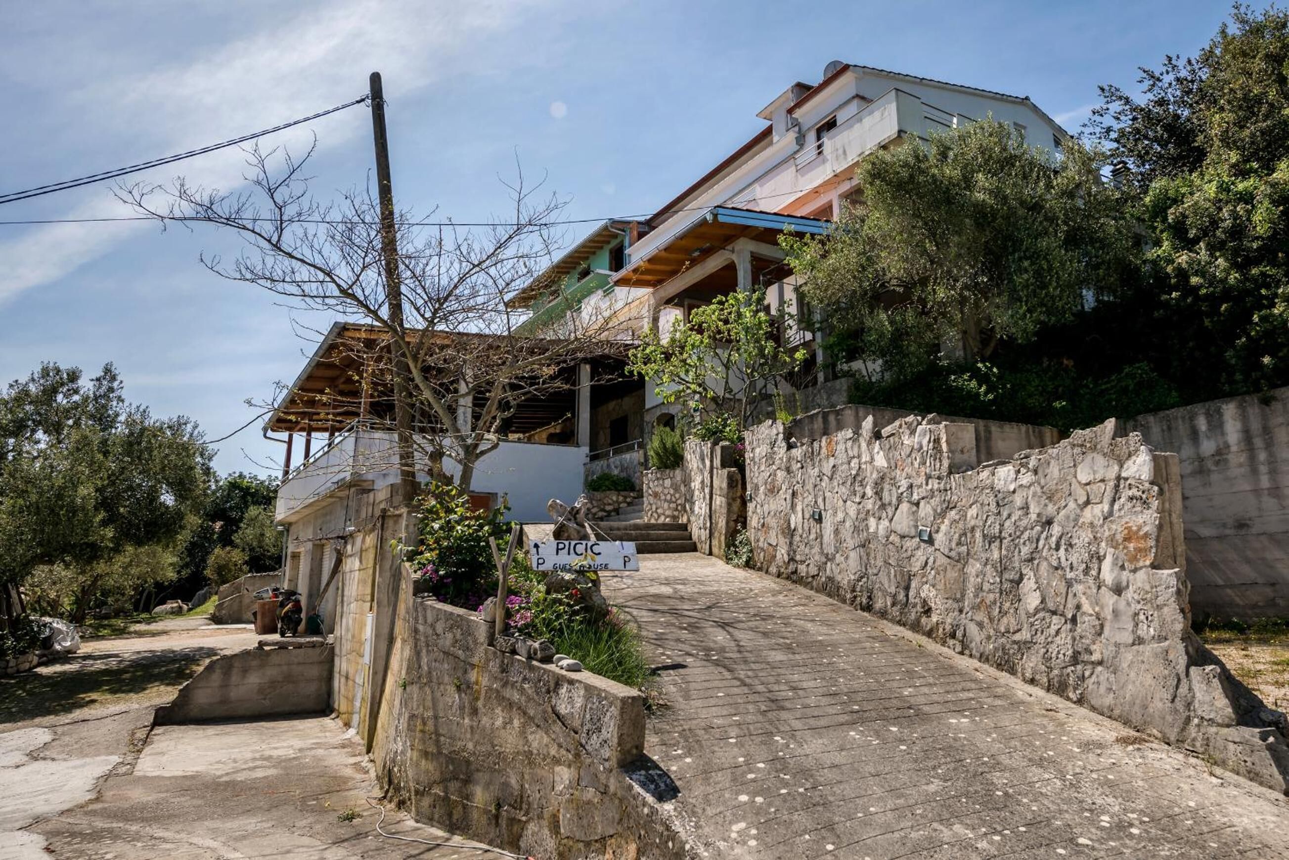 Un edificio residencial con un muro de piedra, un camino pavimentado y un letrero que indica una zona de estacionamiento.
