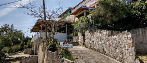 Un edificio residencial con un muro de piedra, un camino pavimentado y un letrero que indica una zona de estacionamiento.