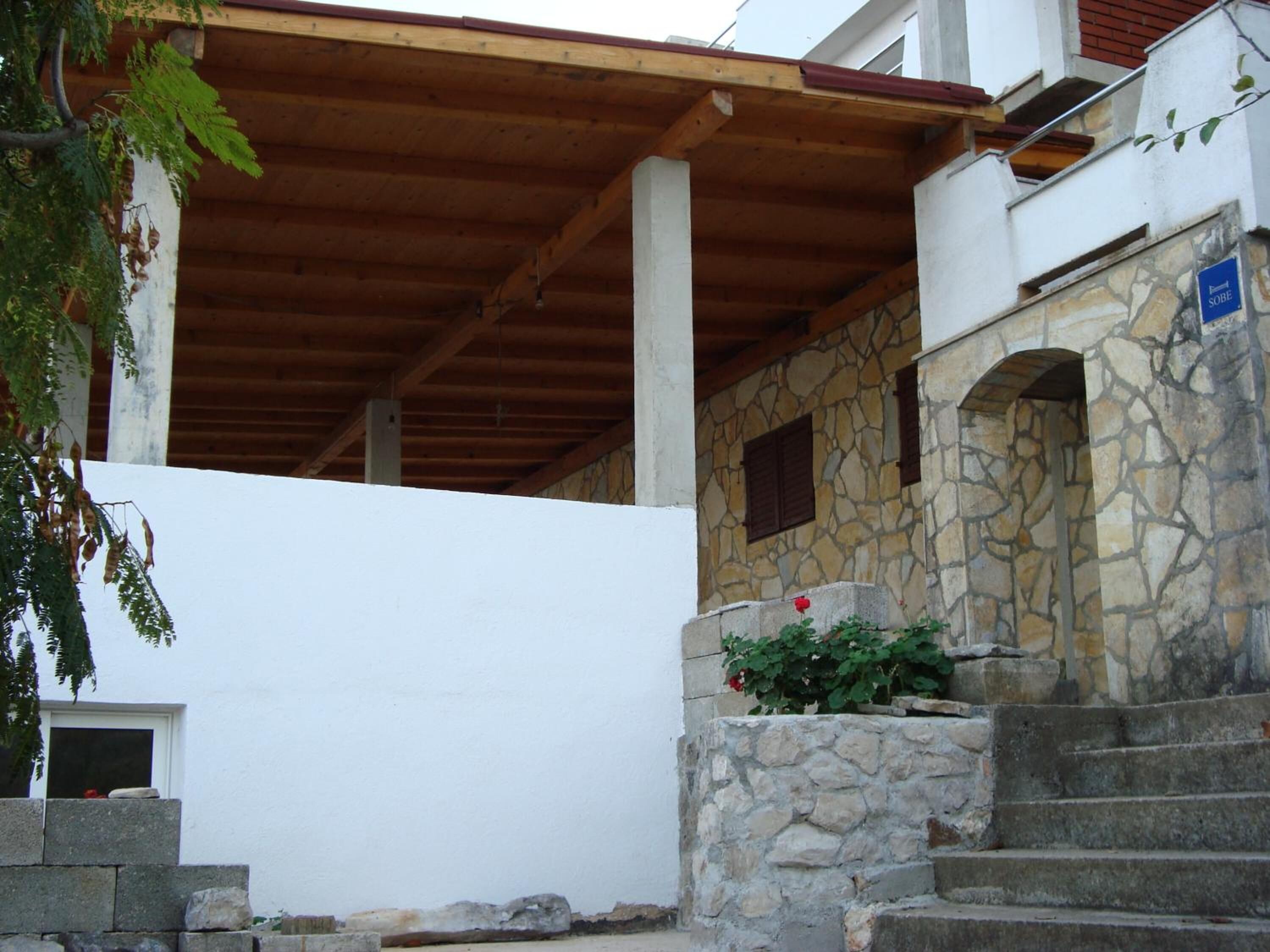 A stone building with a wooden roof, a stone staircase, and a small garden with a red flower.