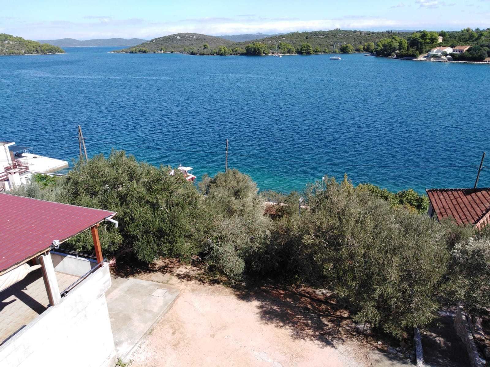 A coastal view with a clear blue sea, a small island, and a building with a red roof.