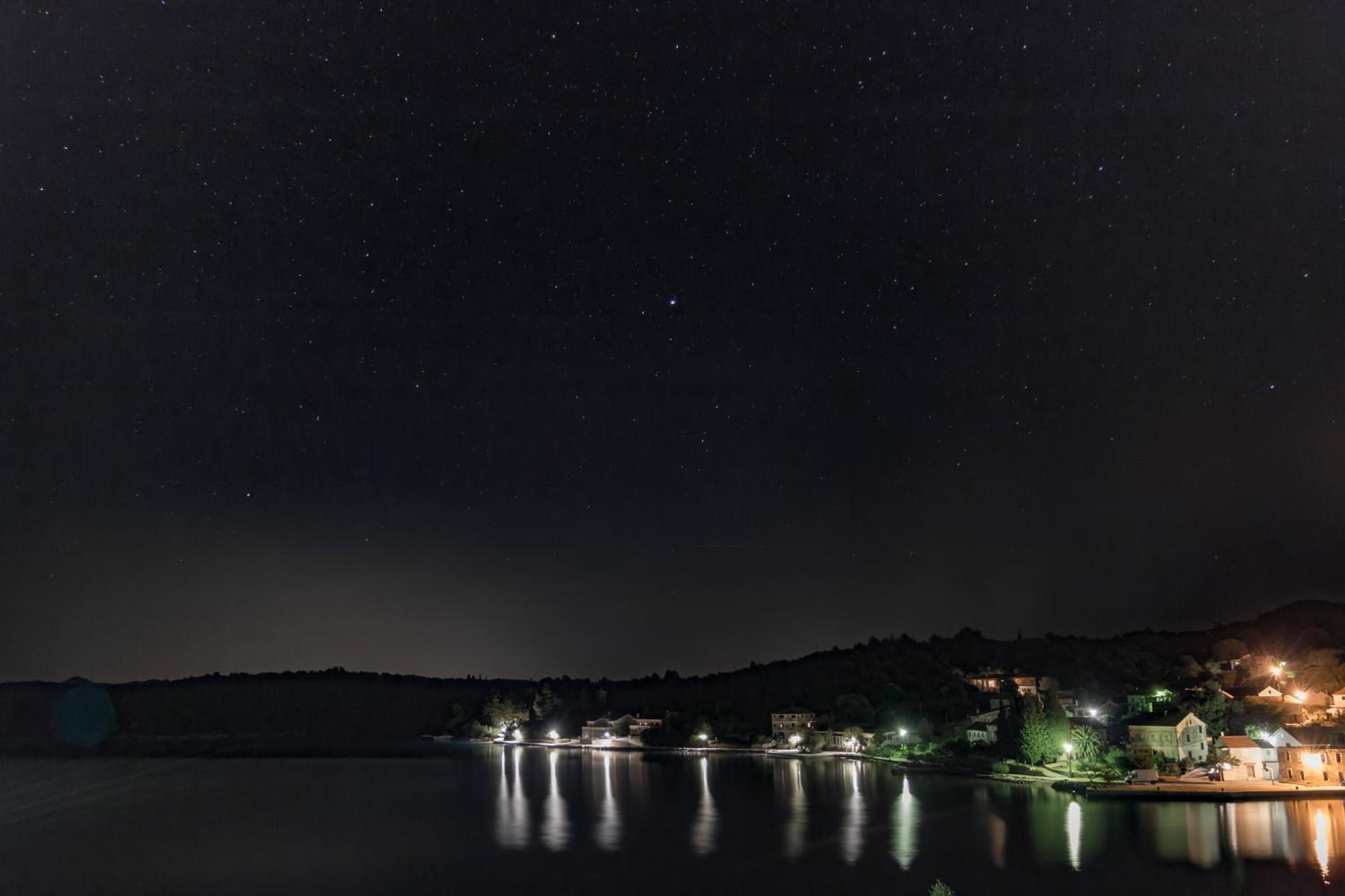 Ein nächtlicher Blick auf den See mit beleuchteten Gebäuden, die sich im Wasser spiegeln.
