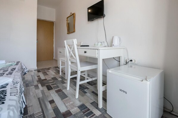 A room with a bed, a desk with a chair, a small refrigerator, a television, and a mirror on the wall. - Picic Guesthouse (Sali)