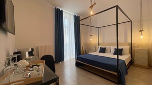 A modern hotel room with a four-poster bed, a desk with a chair, a TV mounted on the wall, and a large window with curtains. - Casa D'Angiò (Manfredonia)