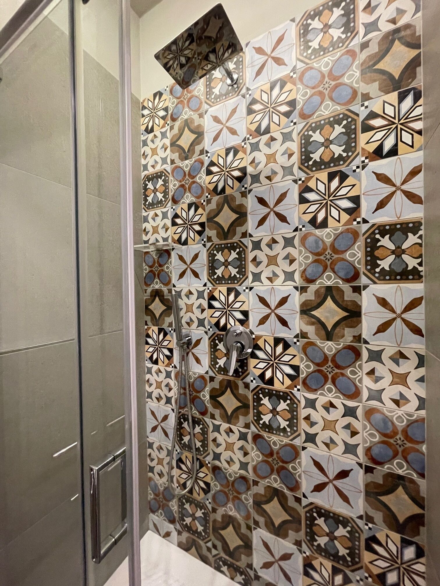 A shower with a glass door and a tiled wall featuring geometric patterns.