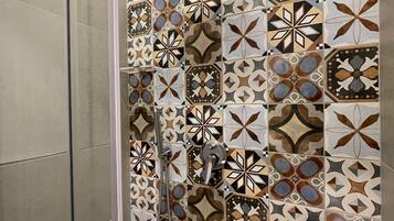 A shower with a glass door and a tiled wall featuring geometric patterns.