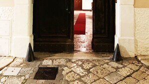 A stone-paved entrance with a dark wooden door, a red carpet, and a metal gate. - Casa D'Angiò (Manfredonia)