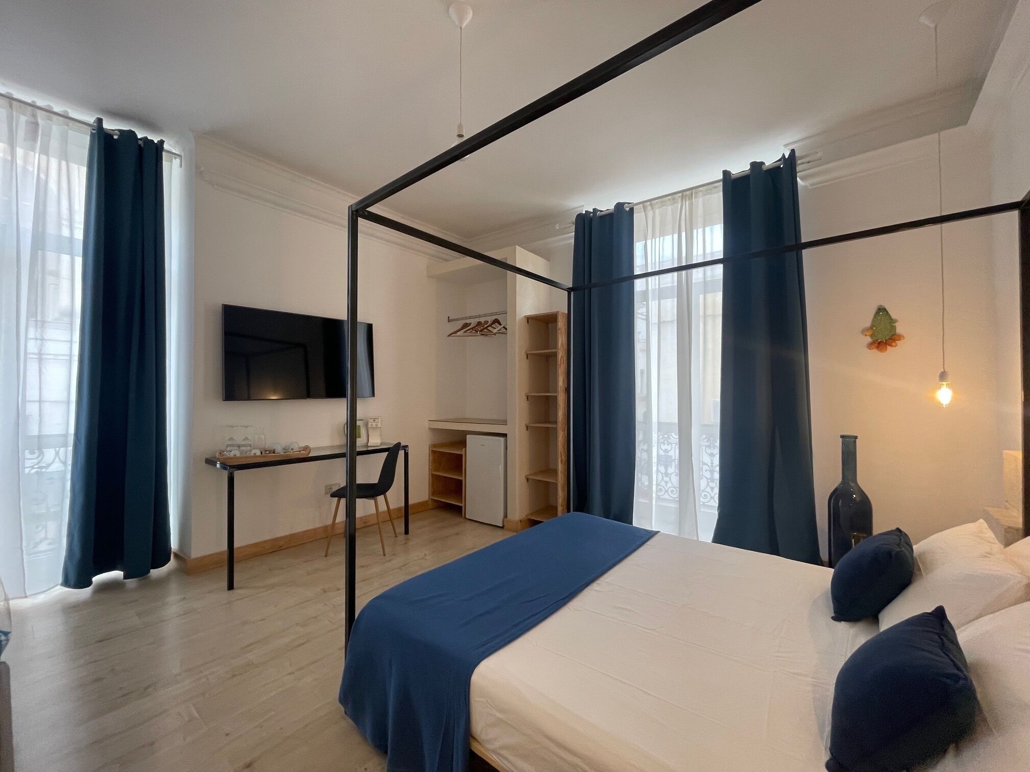 A bedroom with a four-poster bed, a desk with a chair, a television, and a wardrobe.