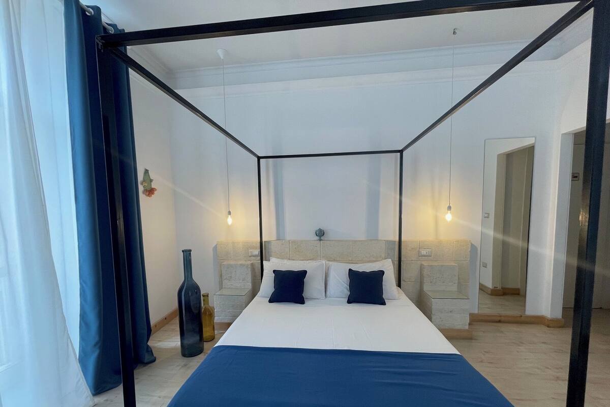 A bedroom with a four-poster bed, a vase, and a mirror.