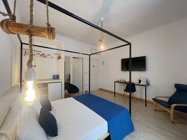 A modern hotel room with a bed, a desk, a chair, a TV, and a hanging light fixture. - Casa D'Angiò (Manfredonia)