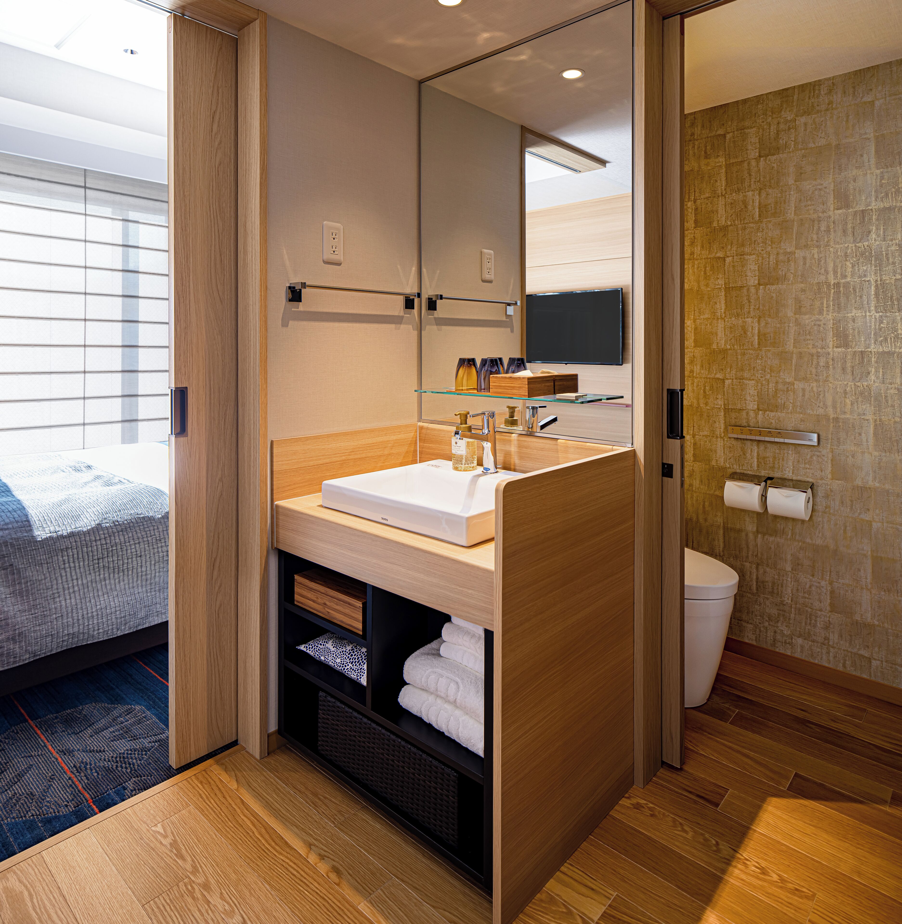 A modern bathroom with a wooden vanity, a glass shelf, a toilet, and a large mirror.