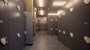 Une rangée de casiers, chacun portant un numéro sur sa porte, un sol carrelé et un plafond équipé de luminaires linéaires.