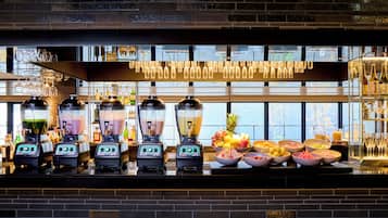 Una zona de bar con varios dispensadores de bebidas, una selección de frutas y una variedad de botellas.