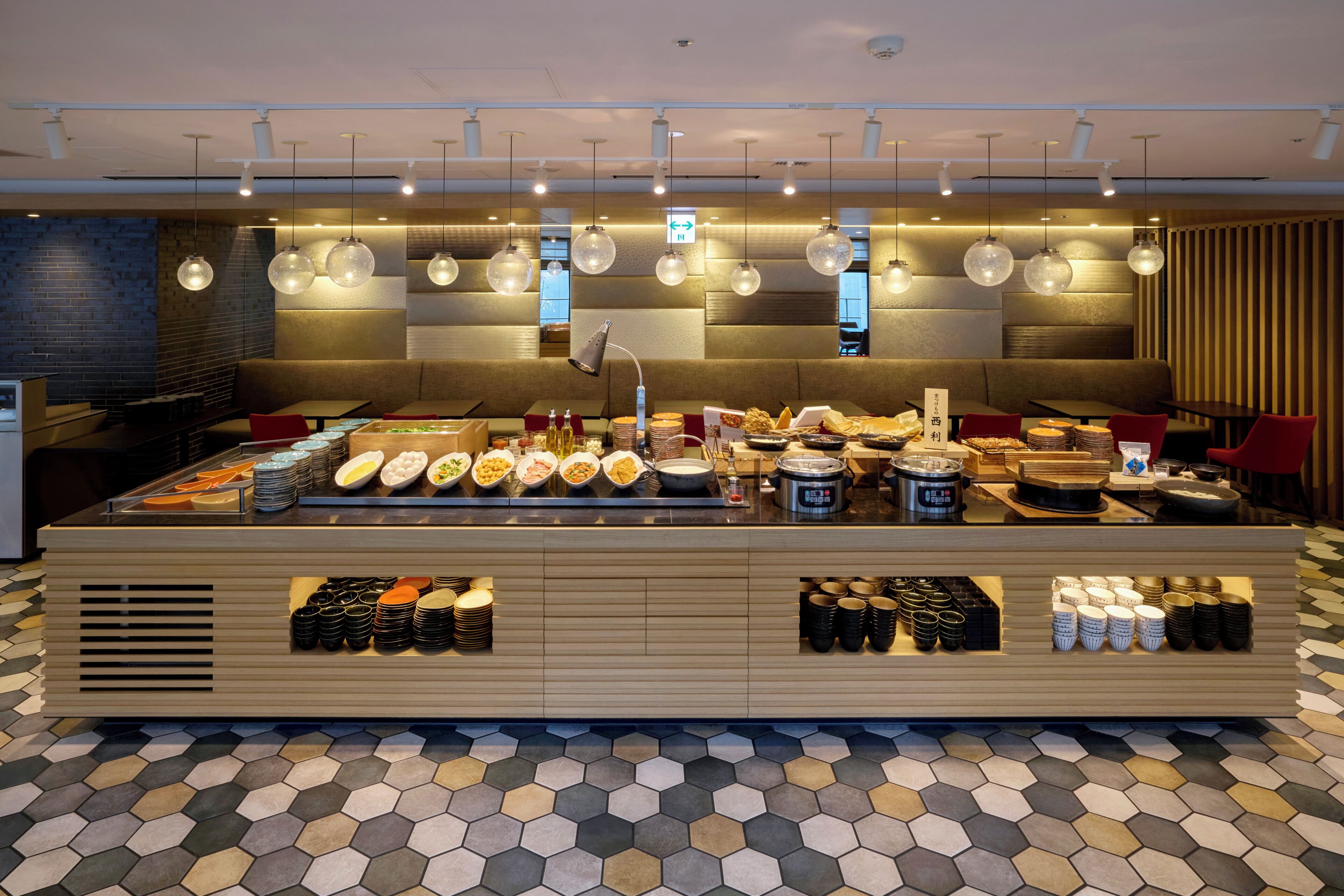 Montaje de bufé con diversas opciones de comida y bebidas, una zona de estar con mesas y sillas, y un suelo con diseño.