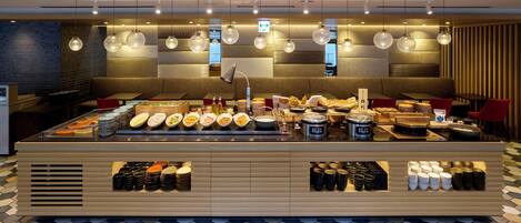 A buffet setup with various food items and beverages, a seating area with tables and chairs, and a patterned floor.